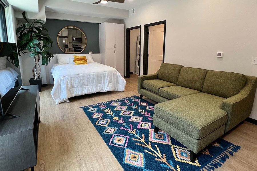 A mirror like the one seen here in a studio at Block 20 Apartments can help a space seem larger by reflecting light. Studio apartment with a sofa, entertainment center, and bed.